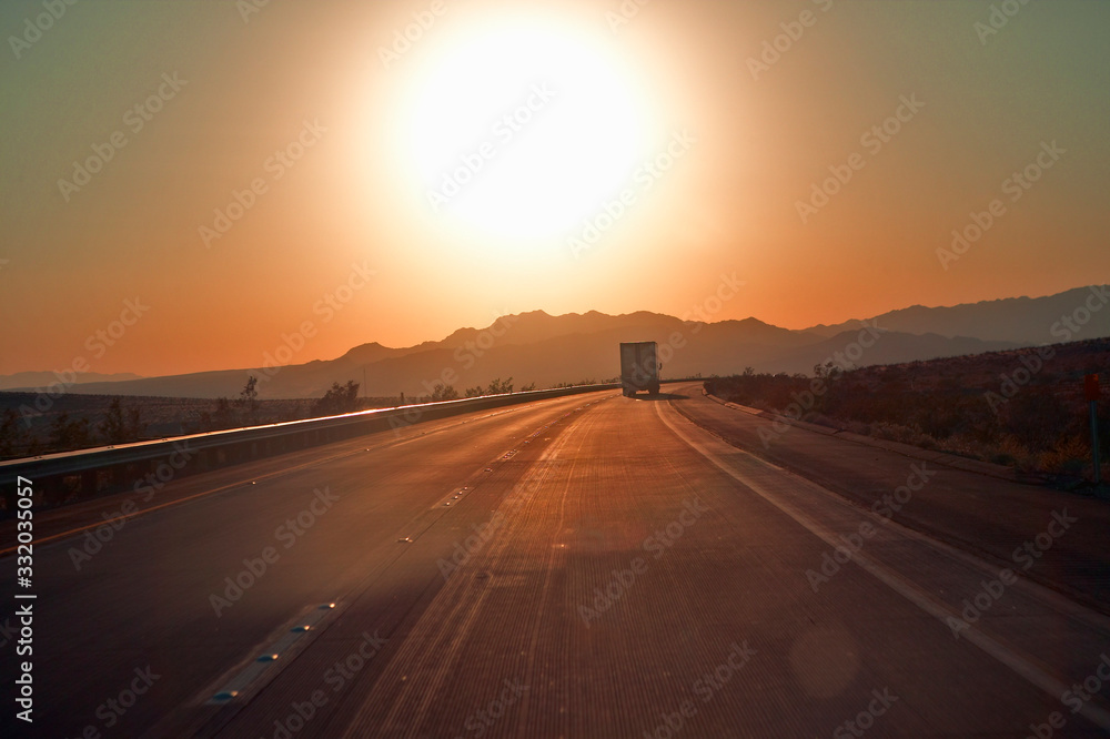 18-wheeler semi-trucks at sunset hit the highway driving down Interstate Highway 15 between Los Angeles and Las Vegas Nevada.