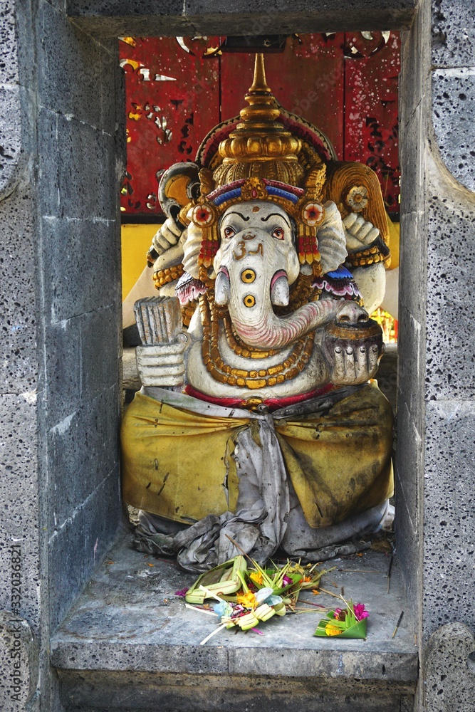 Colorful painted Ganesha statue tucked into an ancient stone niche in Bali Indonesia