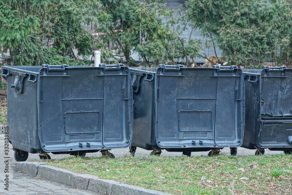 three black plastic trash cans are standing outside in green grass three black plastic trash cans are standing outside in green grass