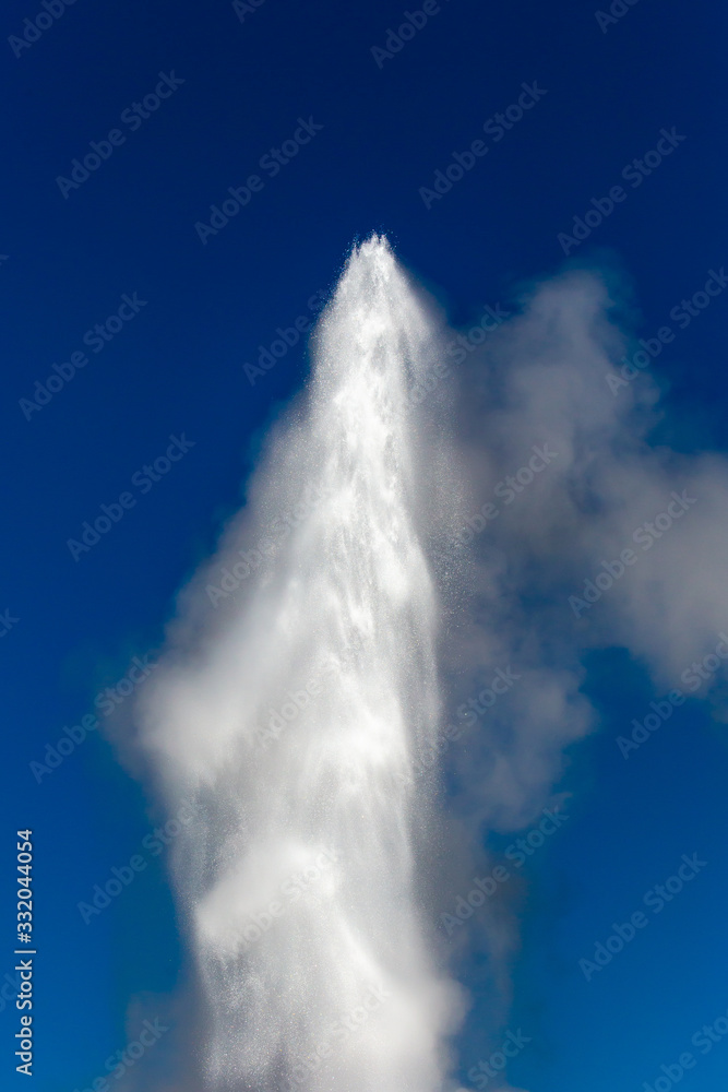 The top of Old Faithful geyser shooting into the air at Yellowstone Park Wyoming with a blue sky