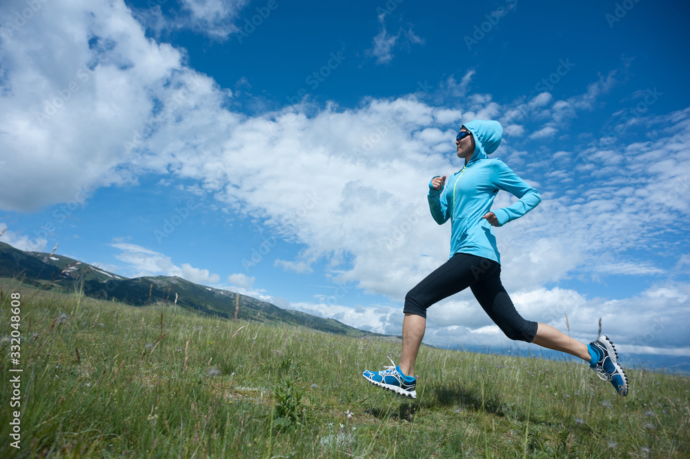 Young fitness woman trail runner running grassland