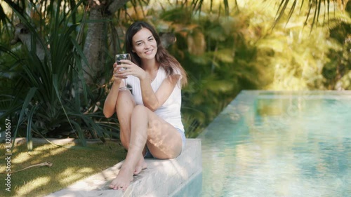 Wallpaper Mural Portrait of woman sits on edge of pool, holds glass of water in hand, smiles Torontodigital.ca