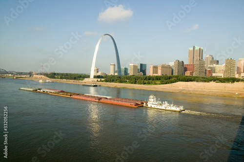Fototapeta Daytime view of tug boat pushing barge down Mississippi  River in front of Gateway Arch and skyline of St