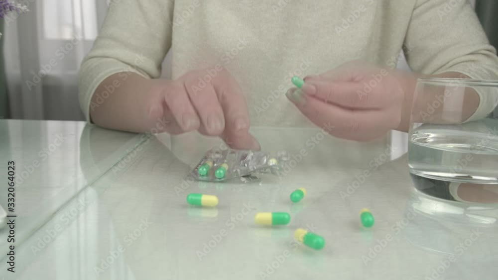young woman in pullover takes coloured pill with trembling hand and drinks water from glass extreme close view young woman in pullover takes coloured pill with trembling hand and drinks water from glass extreme close view