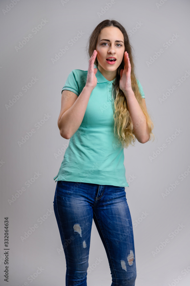 Vertical photo of a surprised pretty young woman with long hair in a turquoise blue jeans blouse on a white background. Vertical photo of a surprised pretty young woman with long hair in a turquoise blue jeans blouse on a white background.