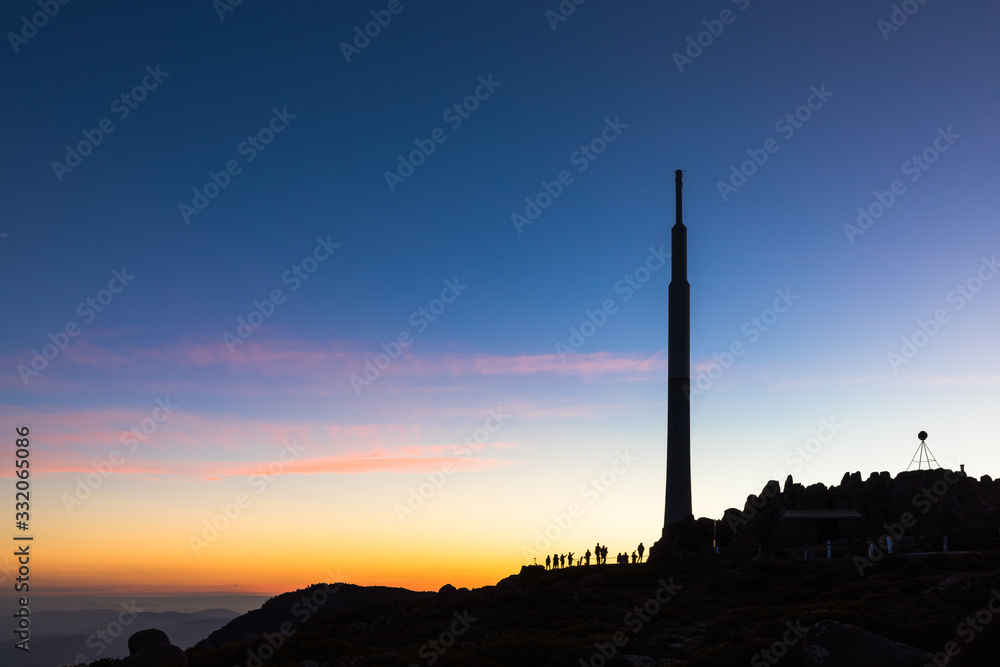 Silhouette of people atop Mount Wellington enjoying the view of Hobart, against a clear blue and pink sky at dusk.  Mount Wellington rises 1,271 metres (4,170 feet) above sea level.