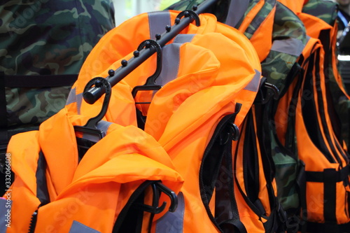 A many bright orange marine life jackets on rack close up, safety on water tourism activity and watersports