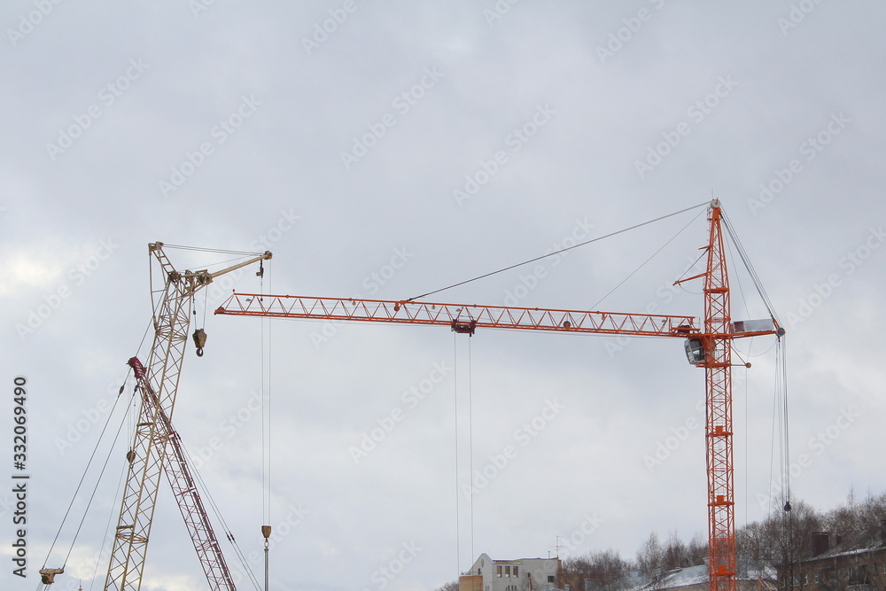 Several construction cranes work at a construction site. Silhouettes against the white sky