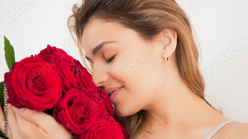 Beautiful woman with red rose flower bouqet. Sensual and attractive female smiling and enjoying flowers at home in bed. Romantic and feminine concept. Handsome portrait shot.