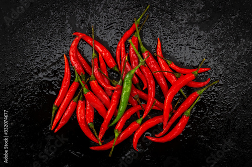 One green chili pepper on red chili peppers on black table