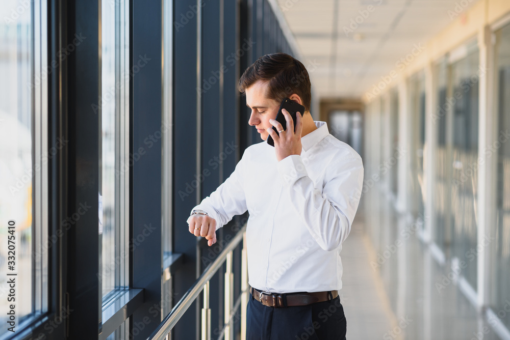 Portrait of a serious confident man boss having mobile phone conversation while resting after meeting with his partners, businessman talking on cell telephone while standing in modern space indoors Portrait of a serious confident man boss having mobile phone conversation while resting after meeting with his partners, businessman talking on cell telephone while standing in modern space indoors