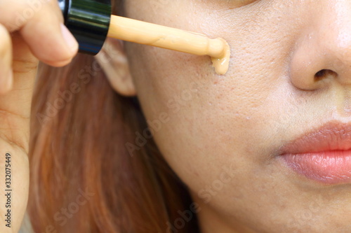 Closeup the Asian woman use pipette drop cosmetic liquid foundation on her cheek skin for hide acne and wide pore on face skin before makeup. Makeup by cosmetic concept.