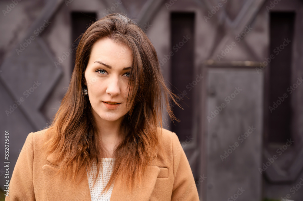 Portrait of a brunette girl standing in spring in a beige coat walk a street on a background of a dark purple wall of a building Portrait of a brunette girl standing in spring in a beige coat walk a street on a background of a dark purple wall of a building