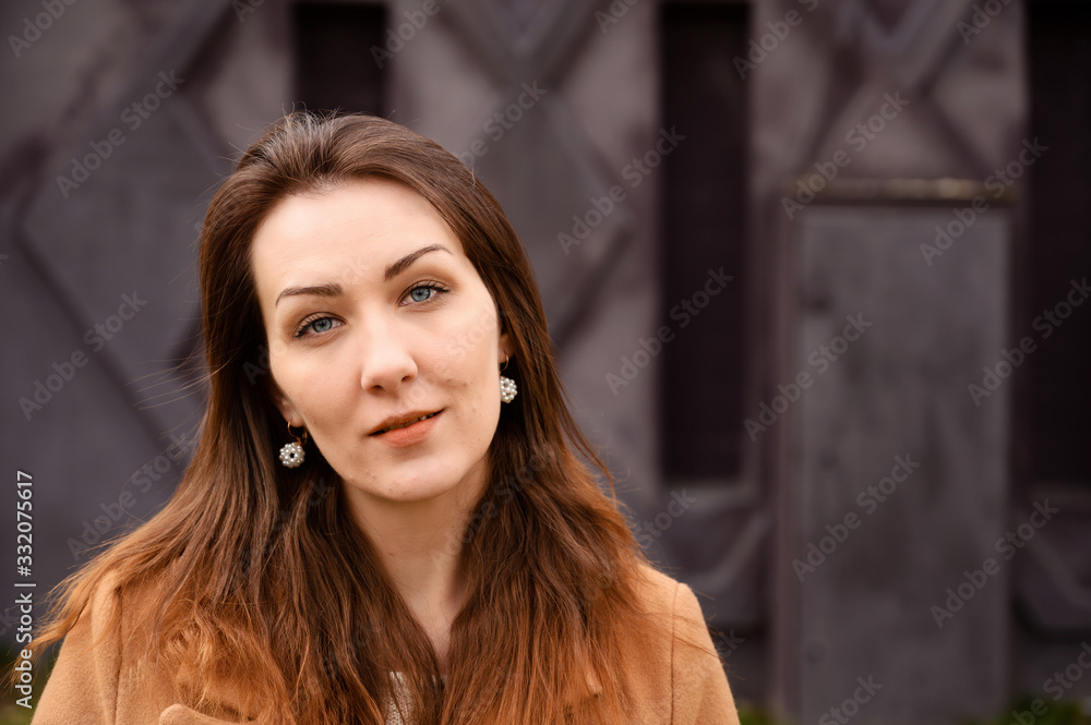 Portrait of a brunette girl standing in spring in a beige coat walk a street on a background of a dark purple wall of a building Portrait of a brunette girl standing in spring in a beige coat walk a street on a background of a dark purple wall of a building