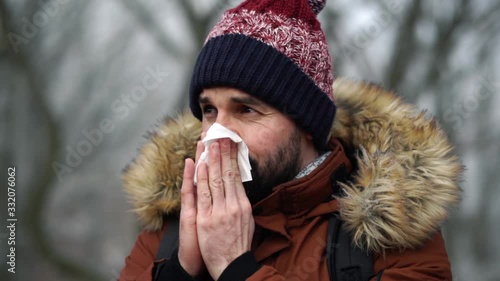 Bearded Caucasian male blows his nose into paper tissue in forest during cold winter day, SLOW MOTION. photo