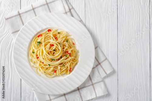Pasta Aglio, Olio e Peperoncino, italian spaghetti with garlic, chili pepper and olive oil on a white plate on a wooden table, close-up, free space, flat lay, horizontal view from above