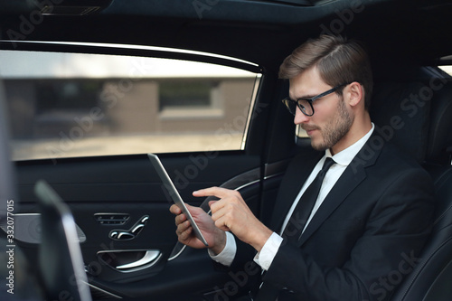 Bilde på lerret Thoughtful young businessman sitting in the luxe car and using his tablet