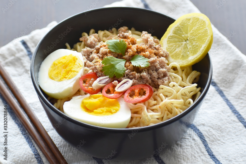 Instant noodles with minced pork, egg, lemon grass, chilli and lemon in a black bowl. Selective focus. Thai style Tom Yum noodles. Instant noodles with minced pork, egg, lemon grass, chilli and lemon in a black bowl. Selective focus. Thai style Tom Yum noodles.