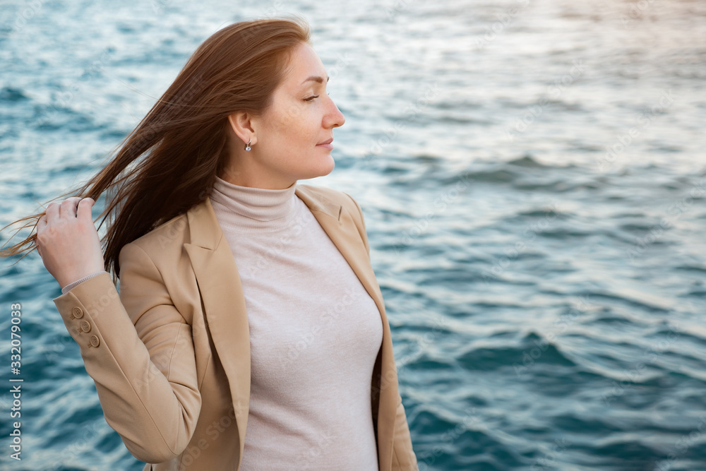 cheerful woman touches long hair standing on waterfront enjoying beautiful nature against rippling sea copy space