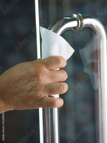 Woman using tissue to hold the door Stainless steel handle to prevent germs protect colona virus, covid 19 