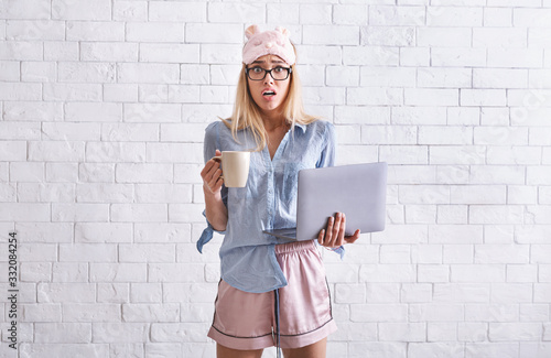 Work from home. Girl in pajamas, sleep mask with cup and laptop