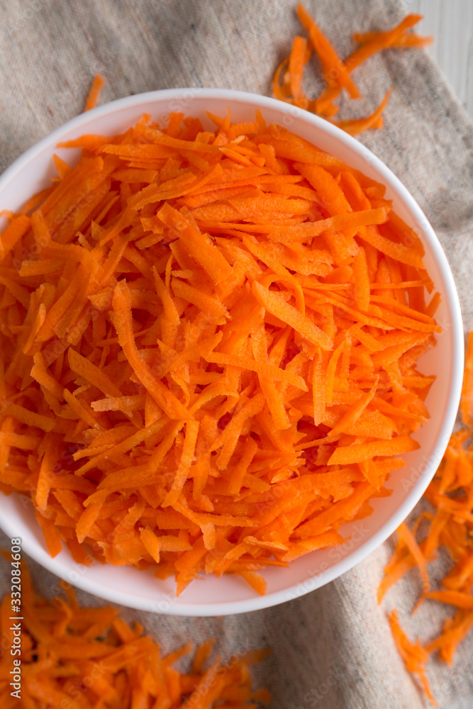 Shredded carrots in a white bowl on cloth, top view. Flat lay, overhead, from above. Close-up. Shredded carrots in a white bowl on cloth, top view. Flat lay, overhead, from above. Close-up.