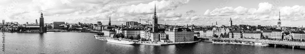 Black and white city landscape of the old town, Gamla Stan island and the city hall on the waterfront of Lake Malaren as seen from Monteliusvagen hill with dramatic clouded sky in Stockholm, Sweden