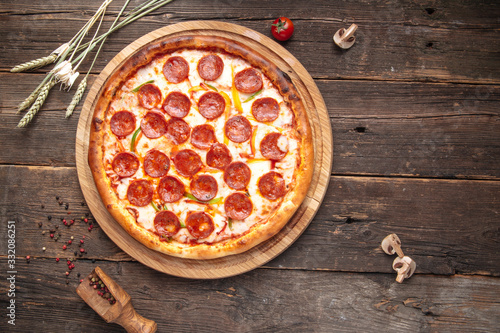 Pepperoni pizza on a wooden round board on a wooden background, top view, horizontal