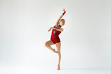 Young gymnast of ballet dancer in red leotard performing beautiful dance on white background, empty space