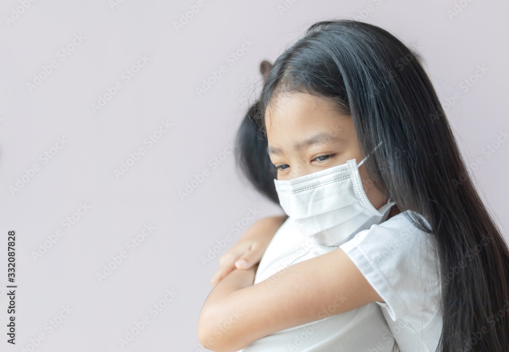 Asian little girl wearing a protective medical mask hugs her mom