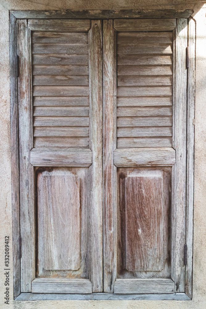 An old, shuttered wooden window with morning sunlight shining from the side on the cement wall in an old house. An old, shuttered wooden window with morning sunlight shining from the side on the cement wall in an old house.