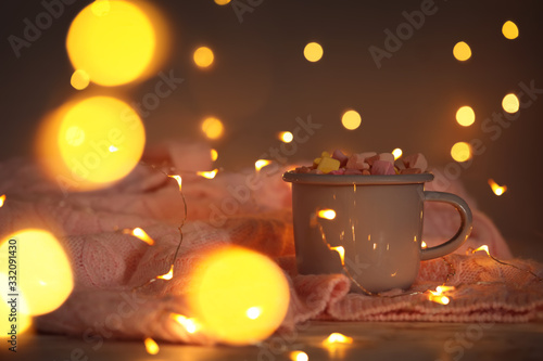 Cup of delicious hot cocoa with marshmallows and fairy lights, bokeh effect
