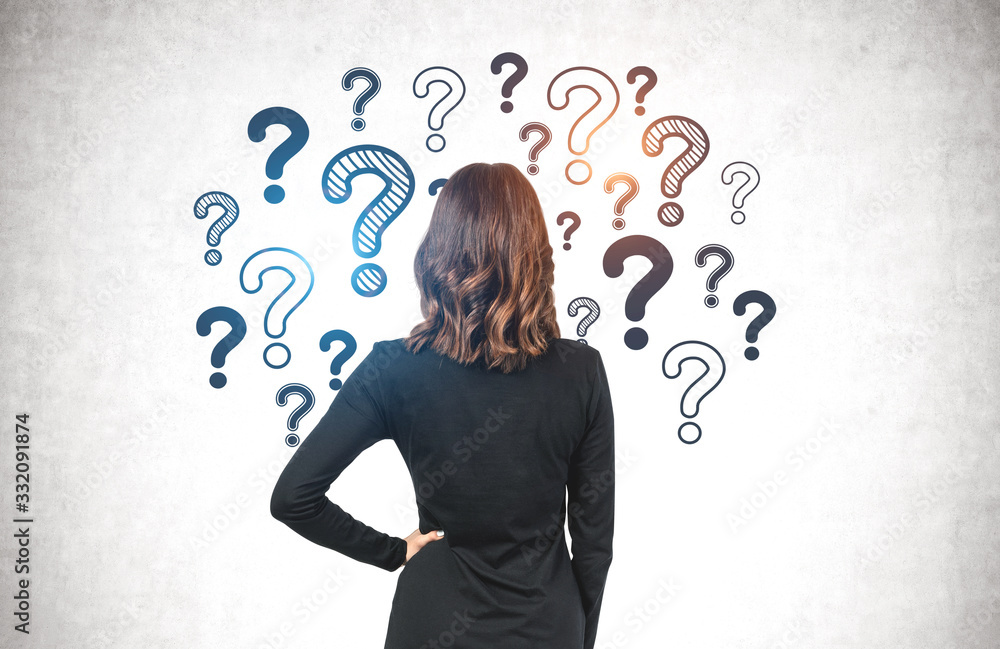 Businesswoman looking at question marks on wall Businesswoman looking at question marks on wall