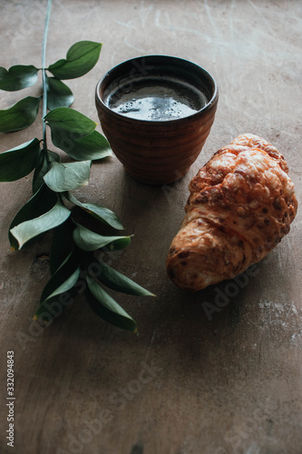 Cappuccino coffee and croissant on wooden background on the table. Perfect breakfast in the morning. Rustic candid style.