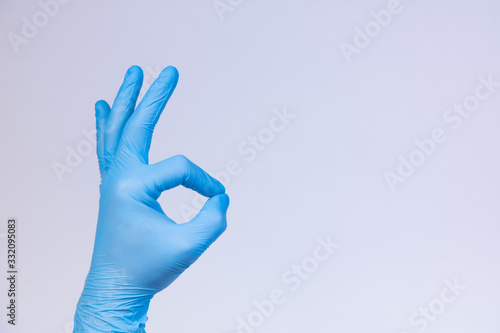Ok sign is showed by left man hand in a blue medical glove on a white background. Okay. All right