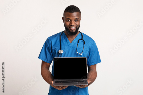 Black cheerful surgeon holding blank laptop screen