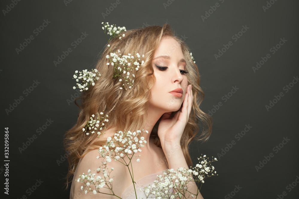 Nice woman with long healthy blonde curly hair, make up and flowers on gray background Nice woman with long healthy blonde curly hair, make up and flowers on gray background