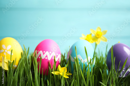 Colorful Easter eggs and narcissus flowers in green grass against light blue background