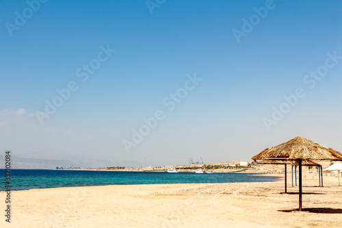 Sandy beach - Japanese Gardens in Jordan. Umbrellas made of dry palm leaves are placed on the white sand. © Mekhanik