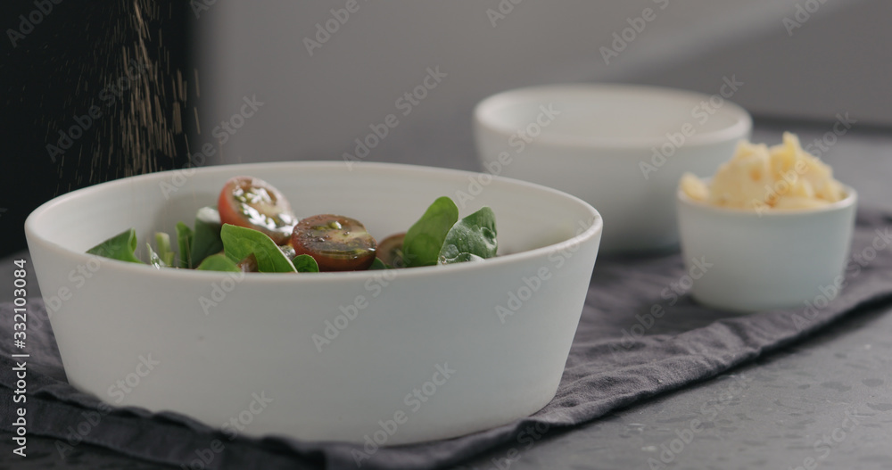 man seasoning salad with kumato tomatoes and spinach in white bowl man seasoning salad with kumato tomatoes and spinach in white bowl