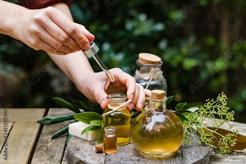 Concept of natural organic oil in cosmetology. Moisturizing skin care and aromatherapy.  Laboratory test outdoor, woman doing reserch and dropping extract from pipette. Wooden background, copy space photo