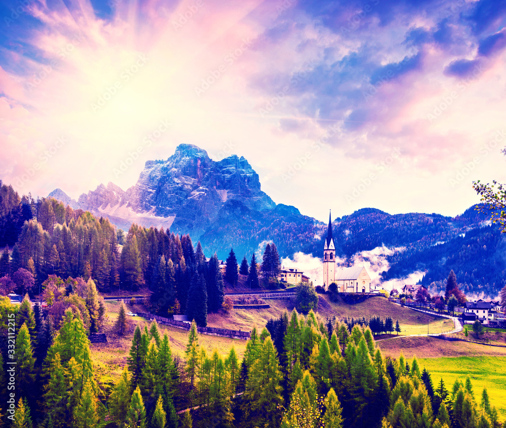 Amazing magical spring unbeatable landscape with the church and yellow larch on a background of mountains in the Dolomites in a sunny day near Codalonga, Alps, Italy.
