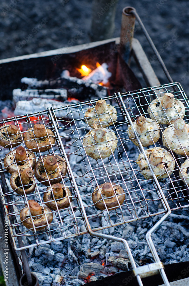 Delicious champignon mushrooms in soy sauce and mayonnaise are fried in grid on grill steam, on homemade grill, closeup