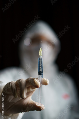 Woman wearing gloves with biohazard protective suit and mask holds an .virus vaccine with syringe, for prevention and treatment from corona virus (Covid-19)