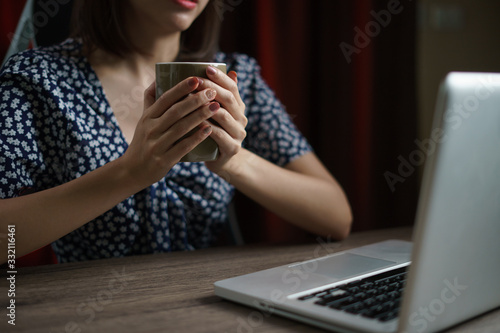 Woman working from home using computer and drinking cup of tea  closeup portrait indoor.