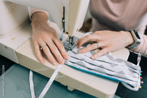 Woman hands using the sewing machine to sew the face home made diy medical mask during the coronavirus pandemia.