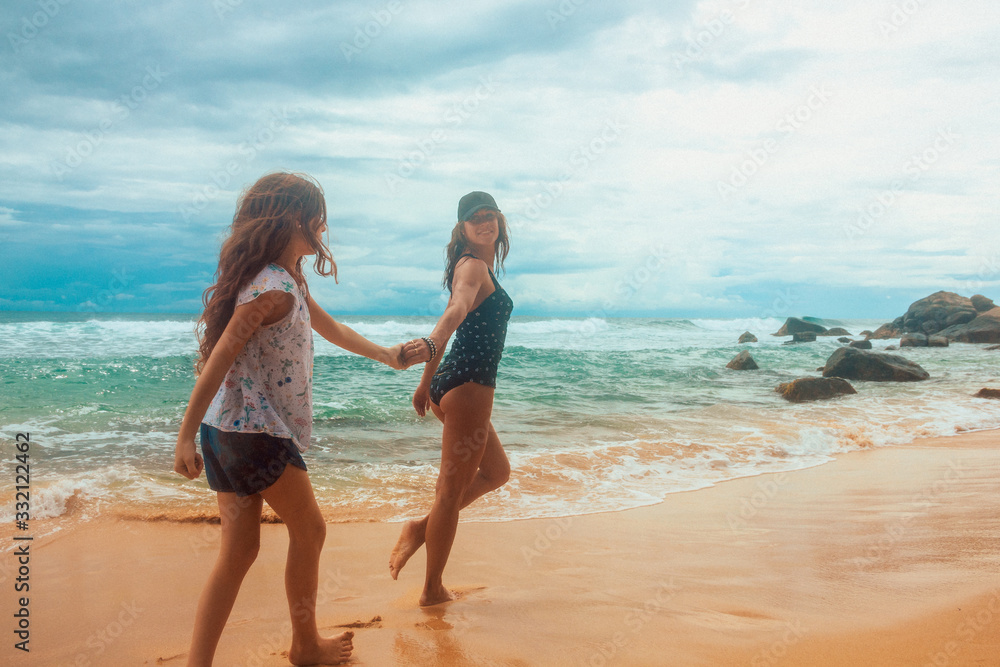 family relationship, mother with daughter are walking on the sunny  beach and smiling. vacation concept, free space