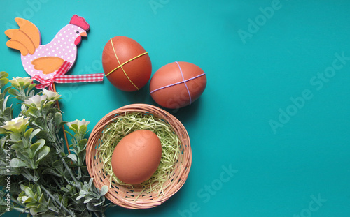 Easter holiday flat lay. Eggs in a nest, flowers and a decorative wooden chicken on a green background. Copy space for your text