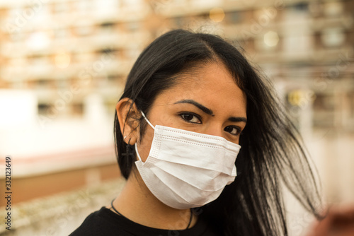 Latin woman looking at the camera with a prevention mask and a defiant look in front of the contagion. Epidemic concept on urban background