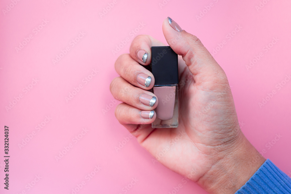 Fototapeta premium The hand of a woman clenching the nail polish on a peach background